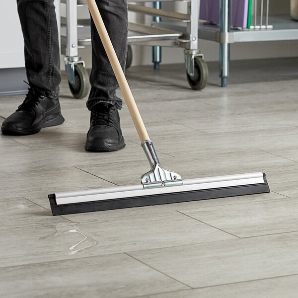 A person using an Ettore aluminum floor squeegee to clean the floor.