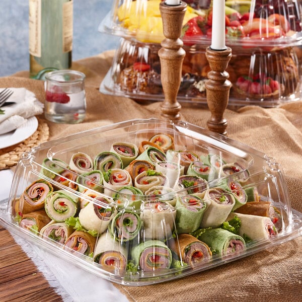 A table with a Sabert clear plastic catering tray of food and a bottle of wine.