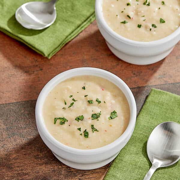 Two bowls of TrueSoups clam chowder with spoons and green napkins.