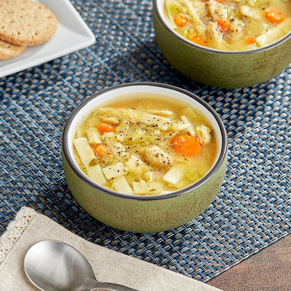 Two bowls of TrueSoups Chicken Noodle Soup on a place mat with a spoon.