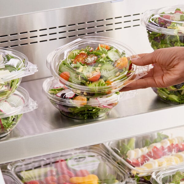 A hand holding a salad in a Choice TamperSafe clear plastic container.