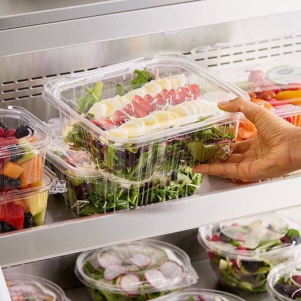 A hand holding a Choice clear plastic rectangular container of salad