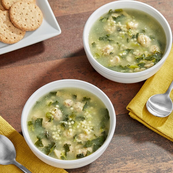 Two bowls of Blount Fine Foods Italian Wedding Soup with meatballs and greens next to a spoon and crackers.