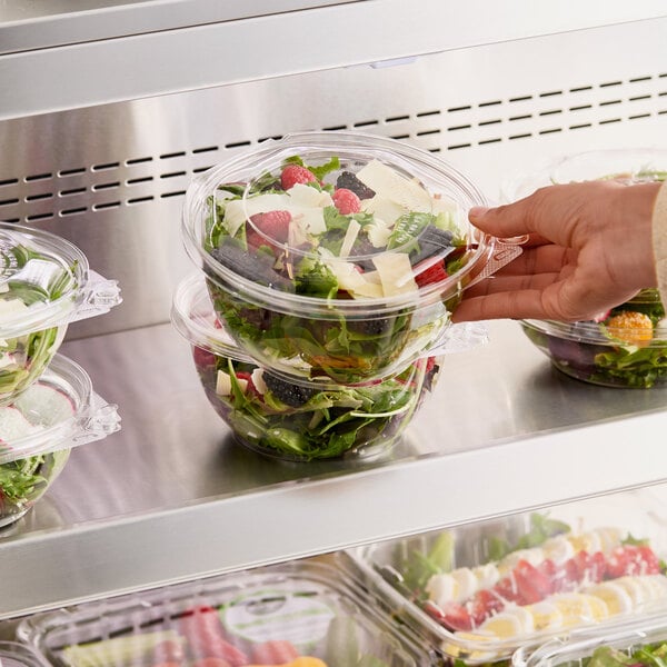 A hand holding a Choice clear plastic bowl of salad with a hinged dome lid.