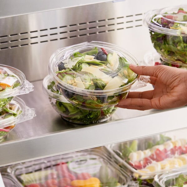 A hand holding a Choice TamperSafe clear plastic bowl of salad.