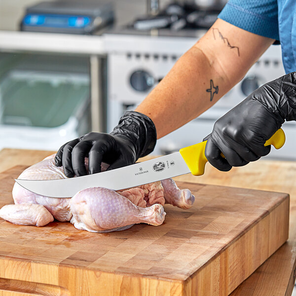 A person in gloves using a Victorinox Breaking Knife to cut a chicken on a cutting board on a counter.
