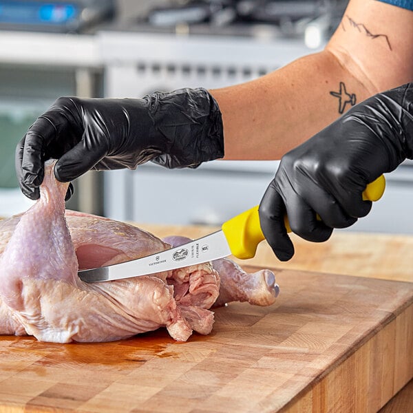 A person in a black glove using a Victorinox curved boning knife to cut meat.