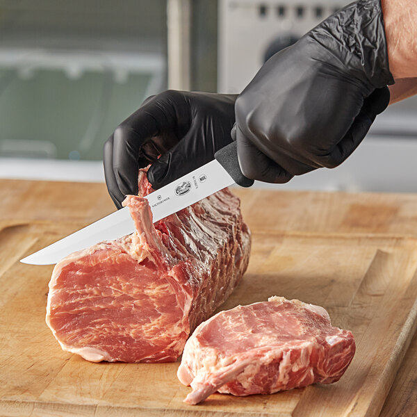 A person in black gloves using a Victorinox fillet knife to cut a piece of meat on a cutting board on a counter.