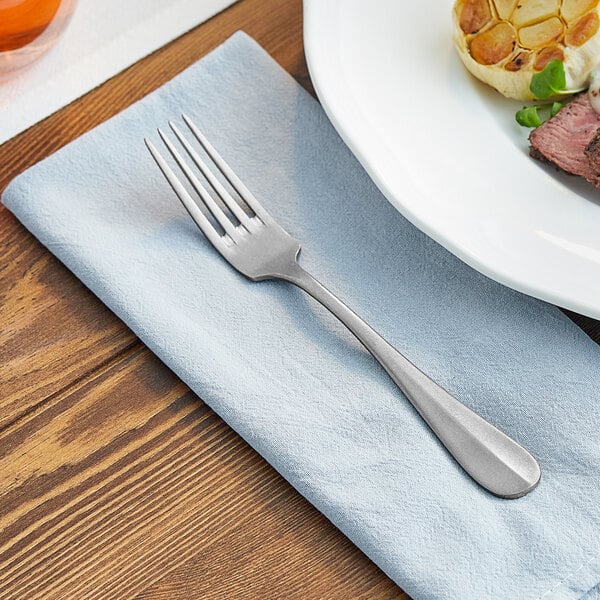 An Acopa Josette stainless steel dinner fork on a napkin next to a plate of food.