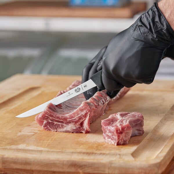 A person using a Victorinox Narrow Boning Knife to cut meat on a cutting board.