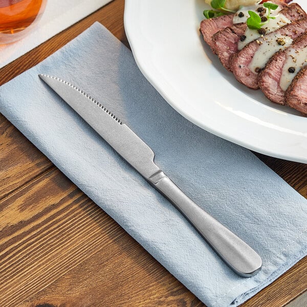 An Acopa Josette steak knife on a plate of meat on a table with a napkin.