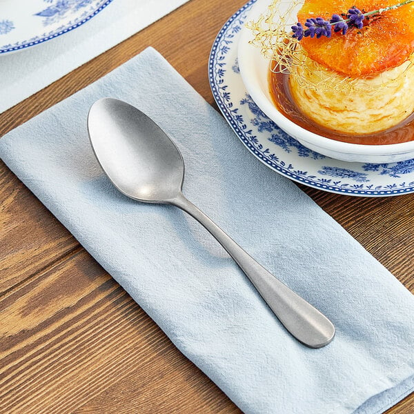 An Acopa Josette stainless steel dinner spoon on a napkin next to a plate of food.