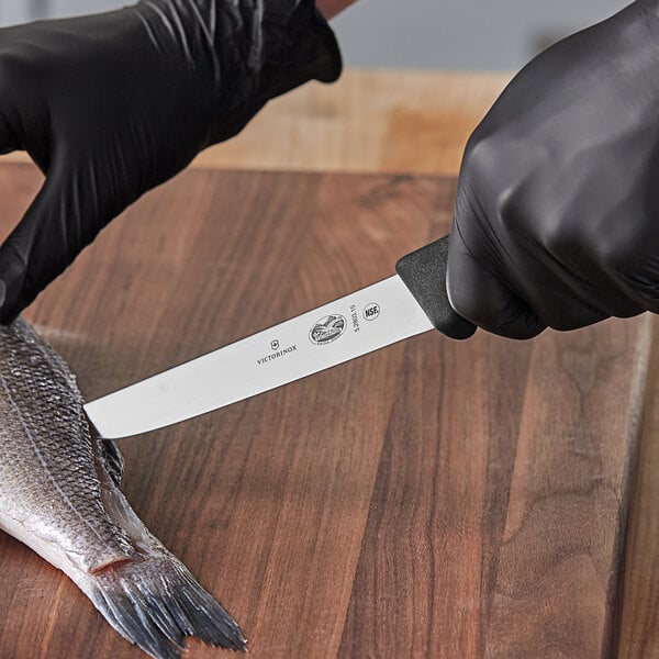 A person in black gloves using a Victorinox fillet knife to cut a fish.