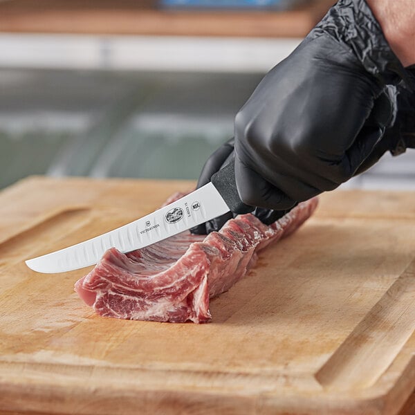 A person in black gloves using a Victorinox curved boning knife to cut meat on a cutting board.