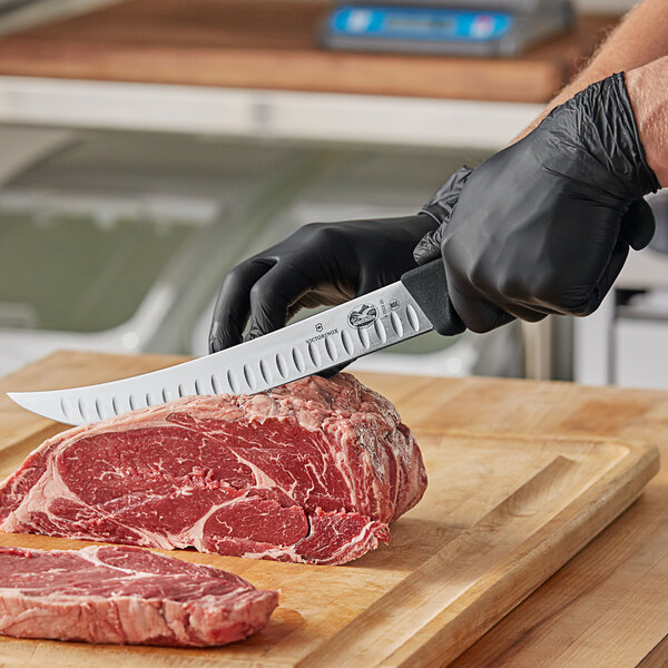 A person wearing black gloves cutting meat with a Victorinox breaking knife.