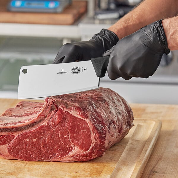 A person in black gloves using a Victorinox cleaver to cut a piece of meat.