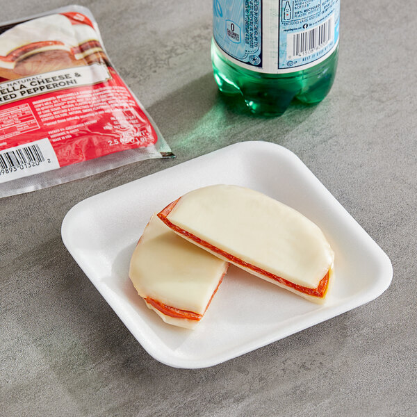 A Cheesewich Pepperoni and Mozzarella cheese sandwich on a plate next to a bottle of soda.