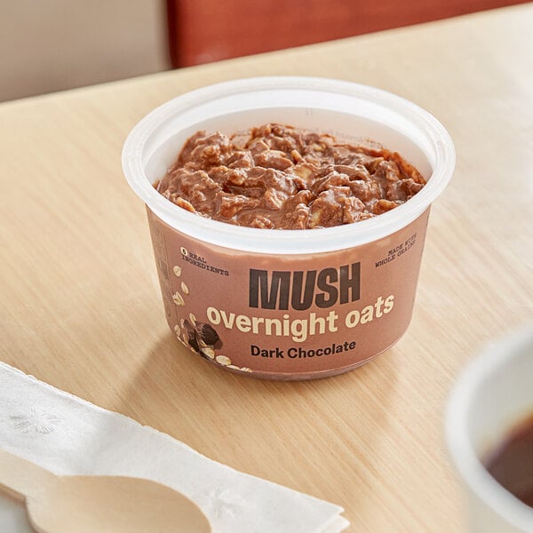 A bowl of chocolate oatmeal on a table with a spoon and a cup of coffee.