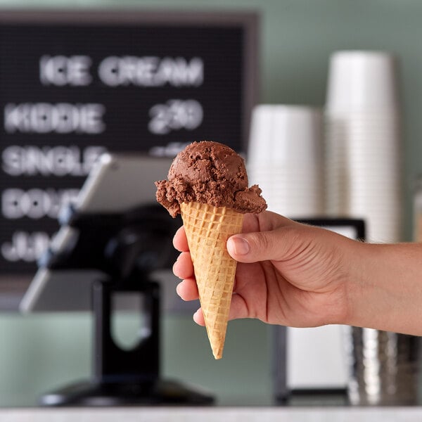 A hand holding a JOY sugar cone filled with chocolate ice cream.