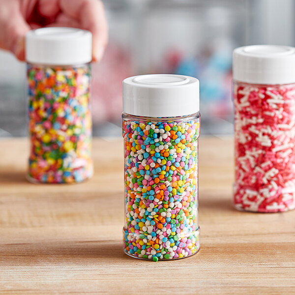 A person holding a round plastic spice container filled with colorful sprinkles with a white lid.