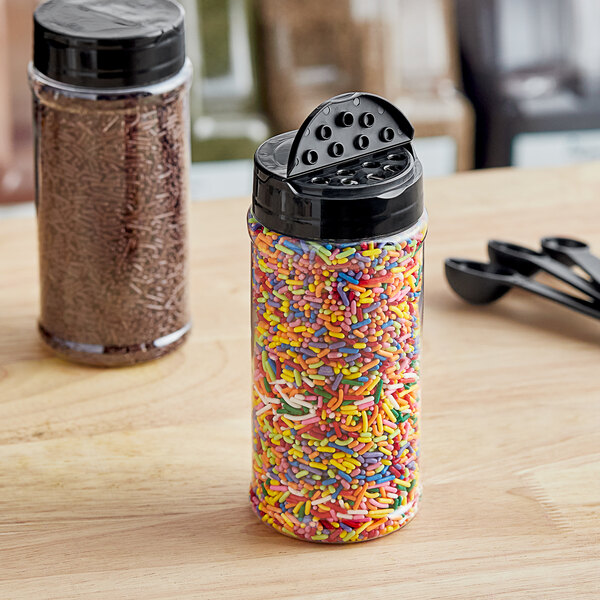 A round plastic jar full of colorful sprinkles with a black lid with 7 holes on a table.