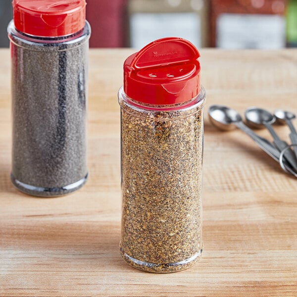 Two round plastic spice containers with red dual flapper lids, each with 3 holes filled with spices.