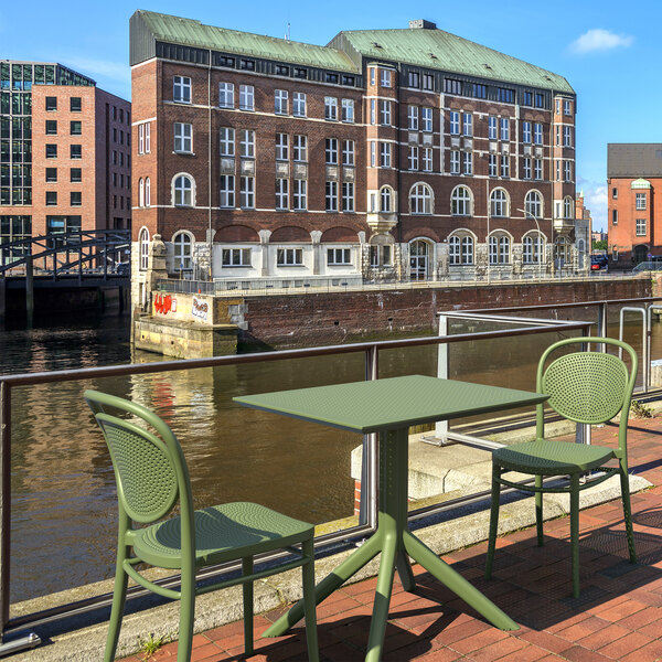 An olive green Siesta Sky square table and chairs on a brick patio.