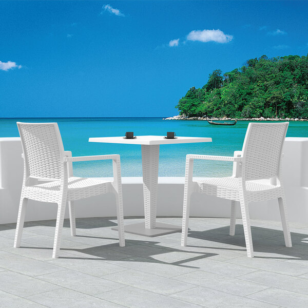A Siesta Ibiza white resin outdoor dining arm chair on a patio overlooking a body of water.