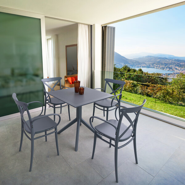 A Siesta Cross XL dark gray resin outdoor dining arm chair at a table on an outdoor patio.