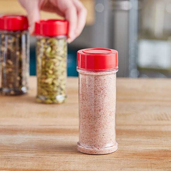 A hand holding a round plastic spice container filled with spices on a home kitchen counter.