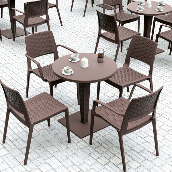 A brown Siesta Capri wickerlook resin outdoor dining arm chair and table on a brick patio.