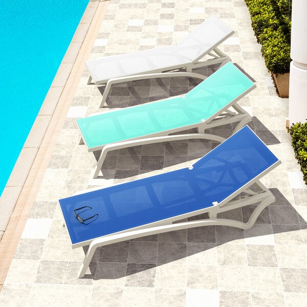 A row of Siesta Pacific white resin outdoor chaise lounges with blue slings next to a pool.