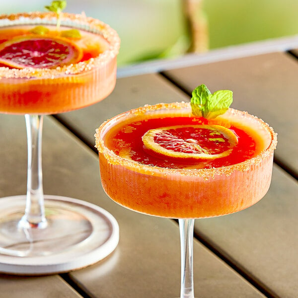 Two glasses of blood orange drinks garnished with slices on a table.