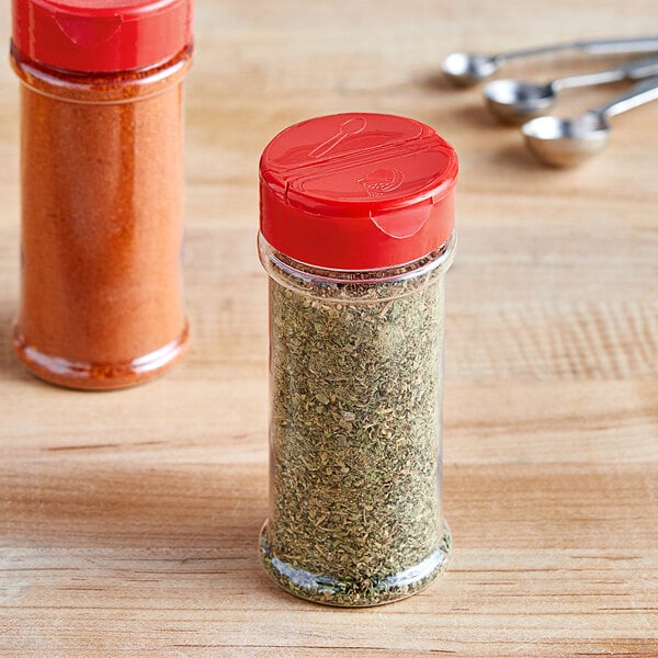 Two red round plastic spice containers with red dual flapper lids with 7 holes filled with spices.