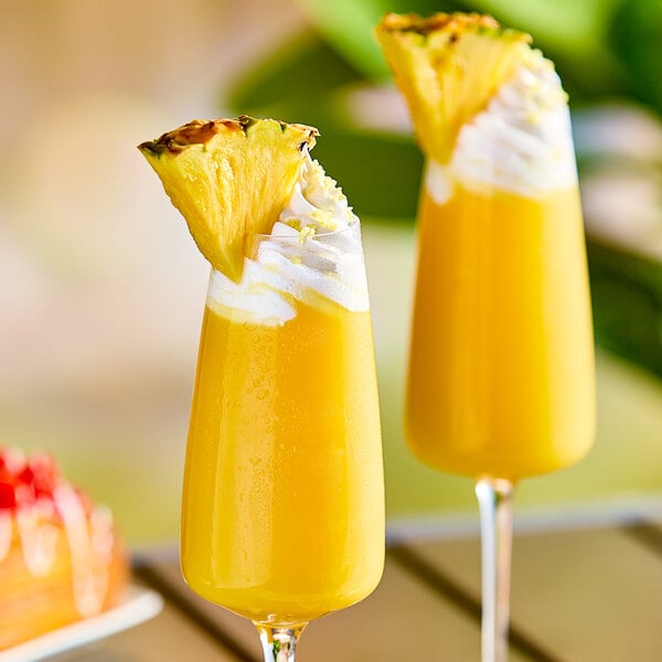 Two glasses of yellow liquid with a pineapple slice on top.