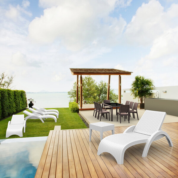 A Siesta Miami white wickerlook resin chaise lounge chair and table on a wood deck.
