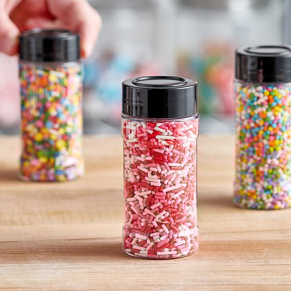 A 4 oz. round plastic spice container filled with sprinkles with a black lid on a table.