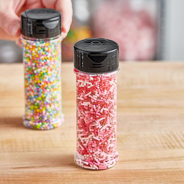 A hand holding a round plastic jar filled with colorful sprinkles with a black flip and sift lid.