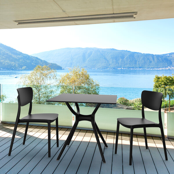 A black Siesta Monna resin outdoor dining chair on a deck overlooking a body of water.