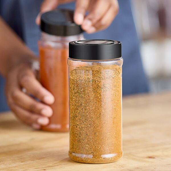 A person pouring spices from a jar into a round plastic spice container.