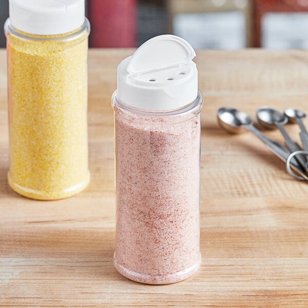 A close-up of two 12 oz. round plastic spice containers with white dual flapper lids.