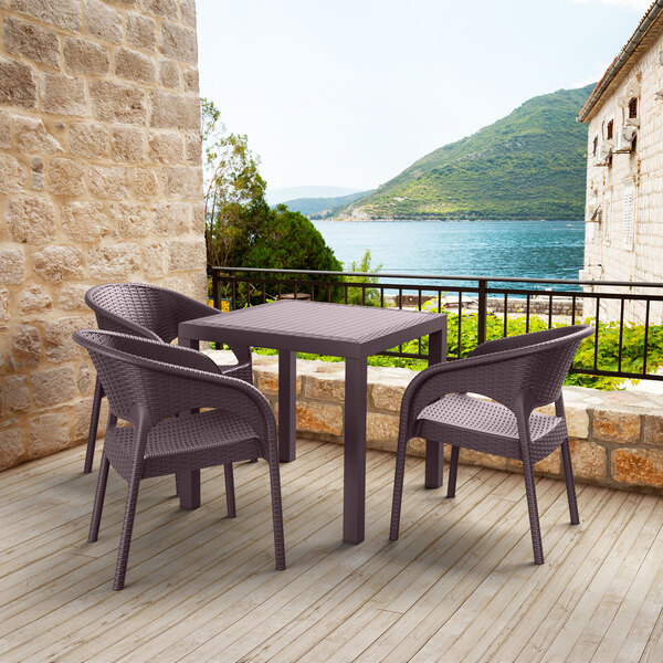 A Siesta Orlando wicker-look table and chairs on a deck overlooking a body of water.