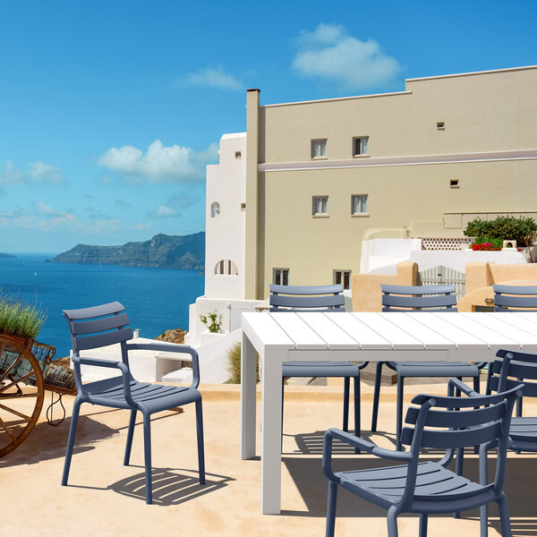 A Siesta Paris dark gray resin outdoor dining arm chair on a table on an outdoor patio overlooking a body of water.