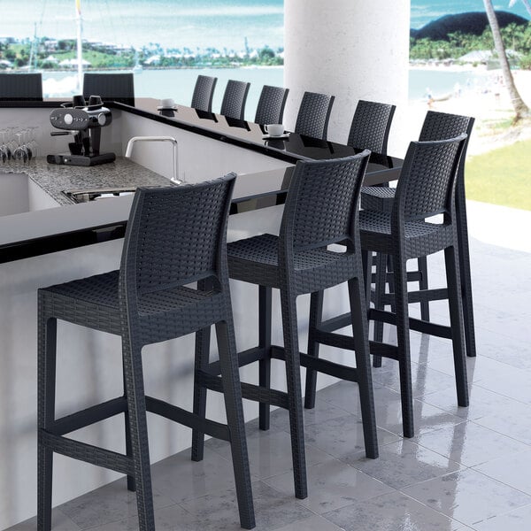 A Siesta Jamaica dark gray wickerlook outdoor barstool on a counter in a cocktail bar.