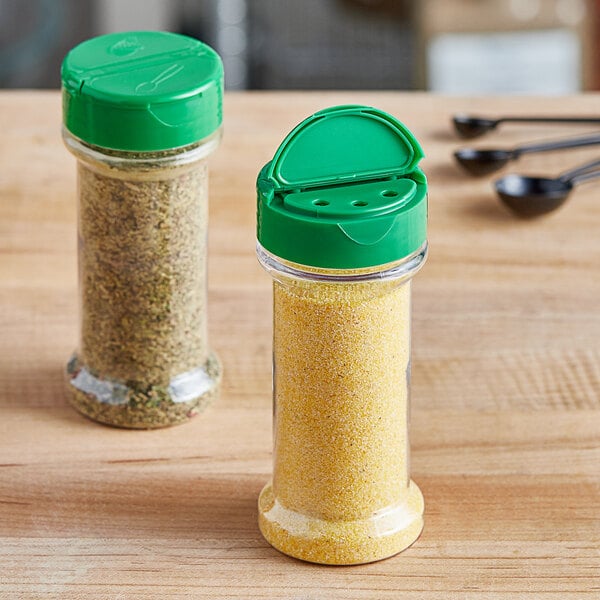 Two round plastic spice containers with green lids on a counter in a home kitchen.