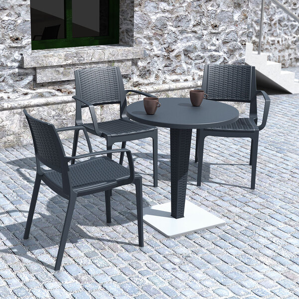 A dark gray Siesta Capri wickerlook resin outdoor dining arm chair on a cobblestone patio table.