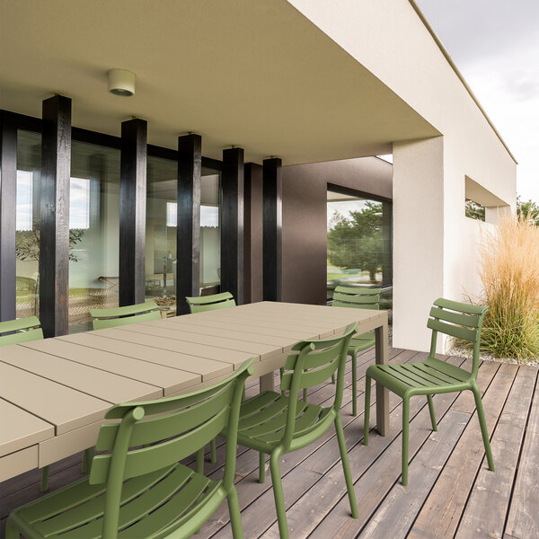 A Siesta Helen olive green resin outdoor dining chair on a wood deck next to a table.