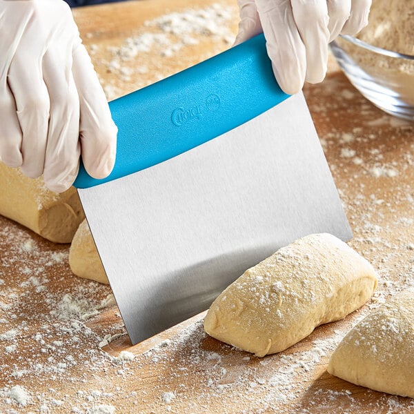 A person in gloves using a Choice stainless steel dough cutter with a blue handle to cut dough on a counter.