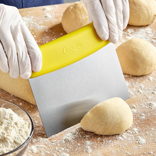 A person using a Choice stainless steel dough cutter with a yellow handle to cut dough on a counter.