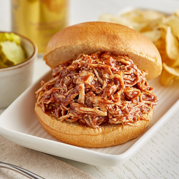 A pulled pork sandwich on a white plate with chips and Ray's No Sugar Added Barbecue Sauce.